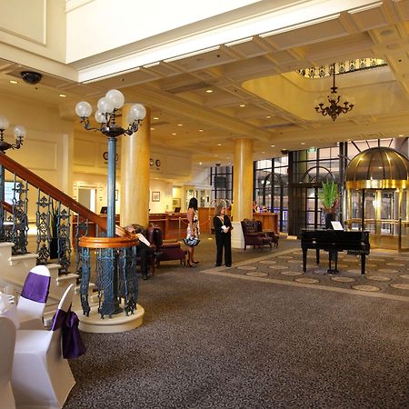 Stamford Grand Adelaide Hotel เกลเนลก์ ภายใน รูปภาพ The photo shows a luxurious interior of a hotel or a restaurant lobby. There is an elegant staircase with ornate railings leading to an upper level. The space features high ceilings with decorative chandeliers and ample natural light coming through l
