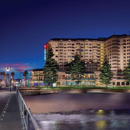 Stamford Grand Adelaide Hotel เกลเนลก์ ภายนอก รูปภาพ The photo shows a waterfront scene at dusk, featuring a large building lit up against a darkening sky. The architecture appears modern and prominent, with several windows illuminated. In the foreground, there is a walkway or pier with fencing along t