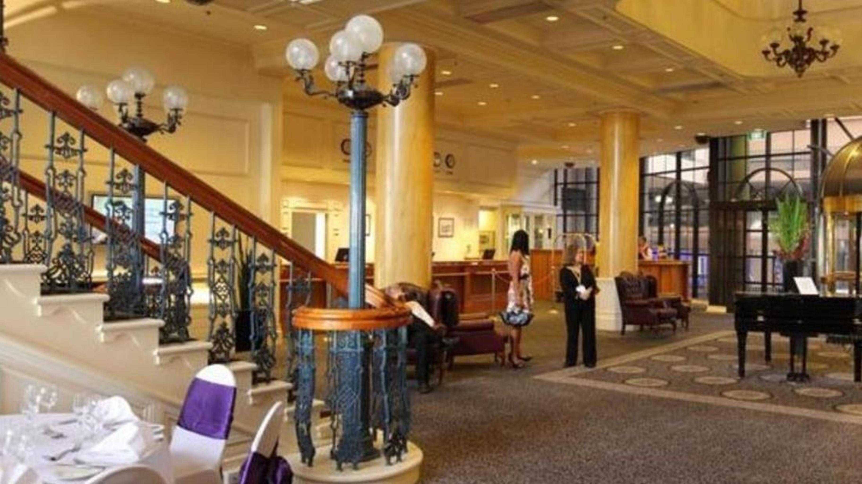 Stamford Grand Adelaide Hotel เกลเนลก์ ภายนอก รูปภาพ The photo shows the interior of a hotel lobby. It features a spacious area with a high ceiling and elegant decor. There is a staircase with a decorative railing leading to an upper level. In the foreground, some guests and staff are present, and ther