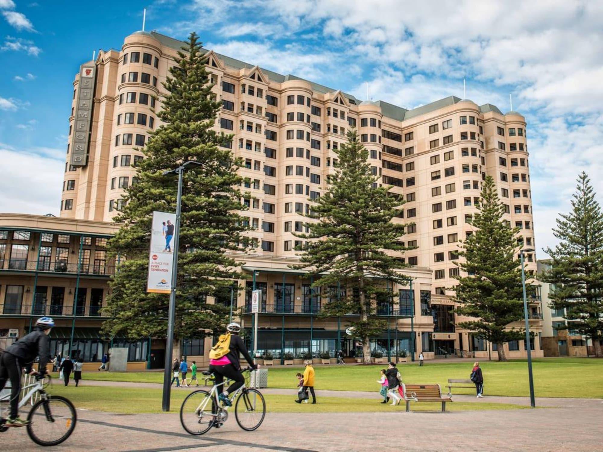 Stamford Grand Adelaide Hotel เกลเนลก์ ภายนอก รูปภาพ The photo depicts a modern building with a large facade, likely a hotel or commercial establishment, situated near a spacious green area. Surrounding the building are several tall trees, providing shade and enhancing the aesthetic appeal. In the fore