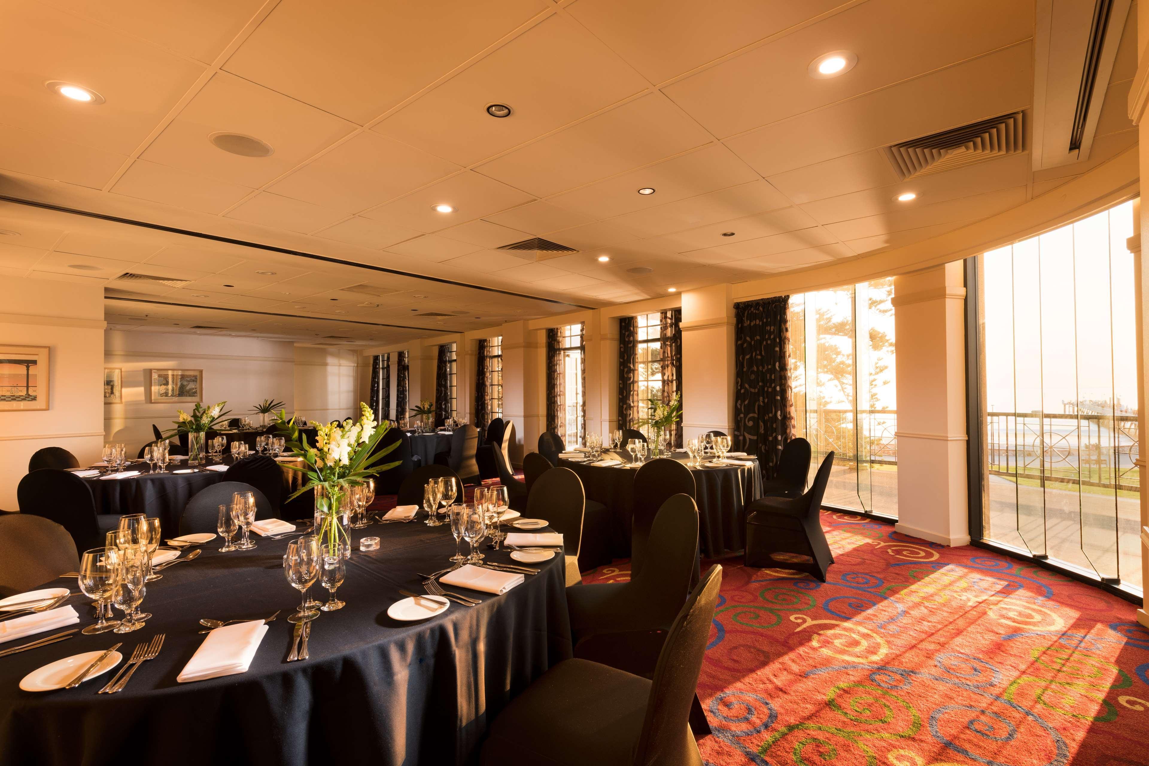 Stamford Grand Adelaide Hotel เกลเนลก์ ภายนอก รูปภาพ The photo shows a well-decorated event space or dining area. There are several round tables draped in dark tablecloths, each set with elegant dinnerware, including glasses and cutlery. The room features large windows that allow natural light to flood